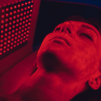 Person receiving red light therapy treatment with a device featuring red LED lights.